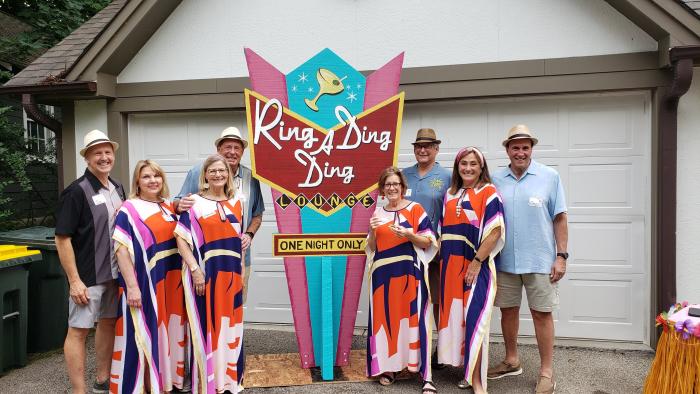 Group posing in colorful retro outfits in front of a Ring A Ding Ding Lounge themed sign