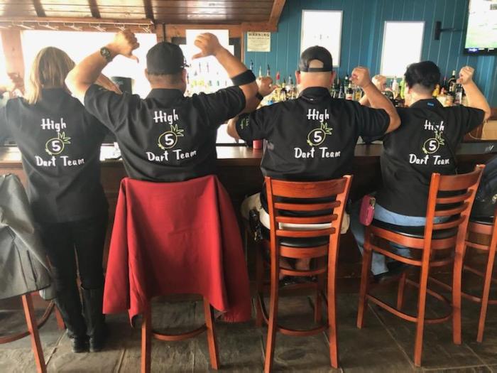Group sitting at a bar showing the back of matching custom dart team shirts