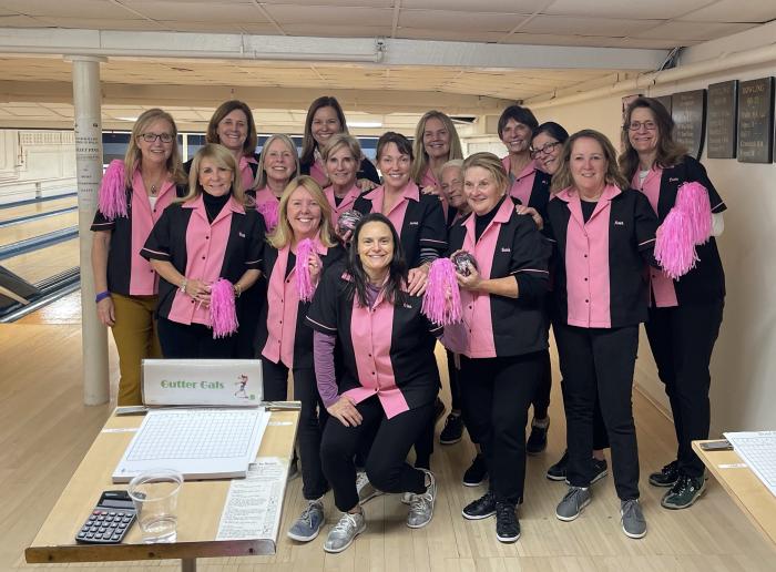 A womens bowling team wearing custom pink and black retro style shirts with pom poms for a team building league event