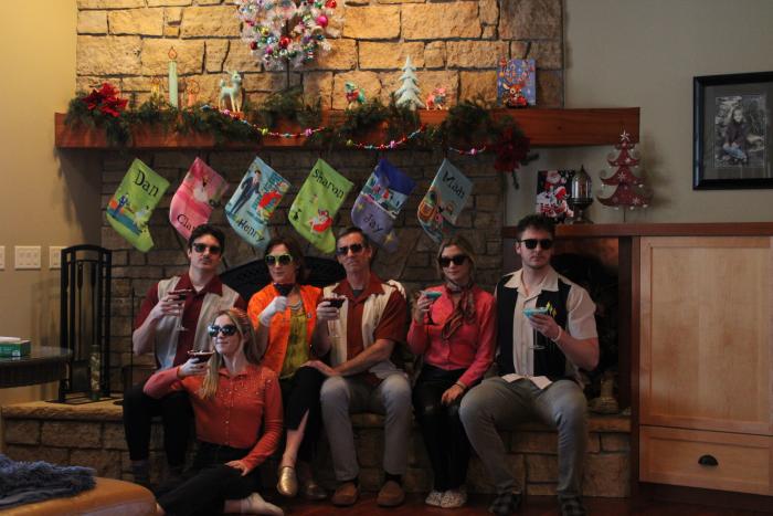Group wearing retro style bowling shirts and sunglasses sitting by a decorated fireplace at a holiday party