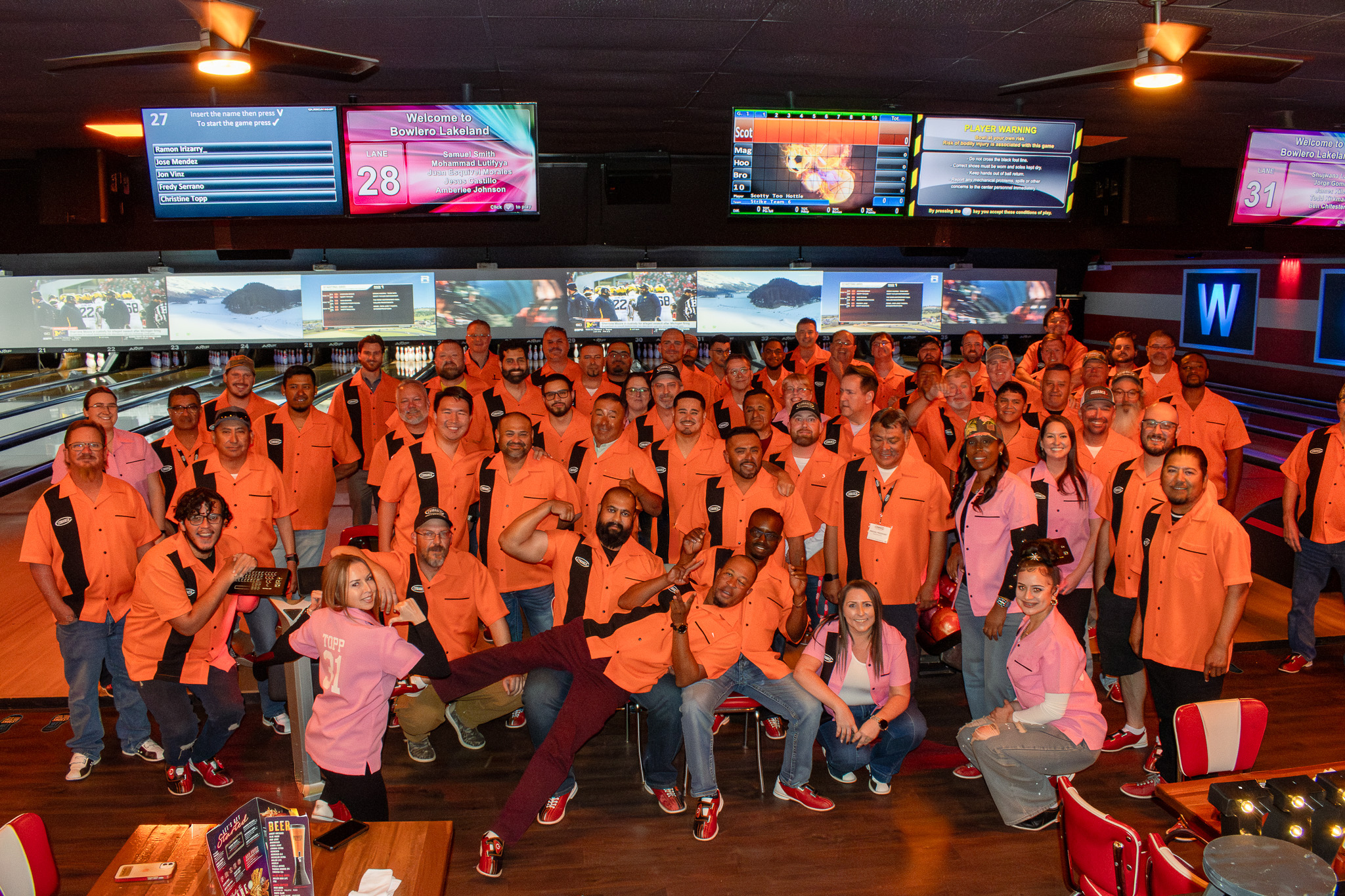 Large bowling league wearing custom orange and black shirts at Bowlero Lakeland – USA made custom bowling shirts