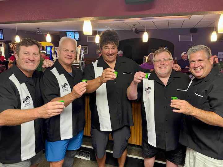 Five men at a bar wearing custom men's bowling shirts raising shot glasses